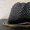 Detalle del bolso de efecto cuero trenzado negro y su cadena dorada