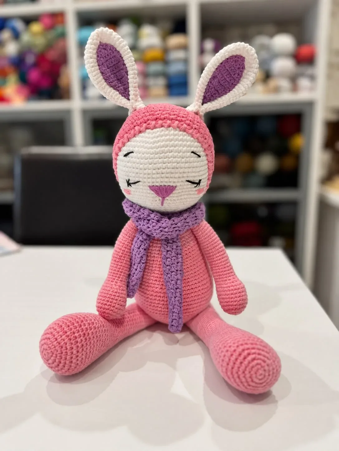Amigurumi de conejita de crochet rosa con bufanda lila en el estudio de malla-lalana